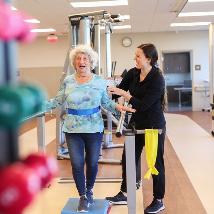 Young nurse smiles as she helps elderly woman in physical therapy exercises