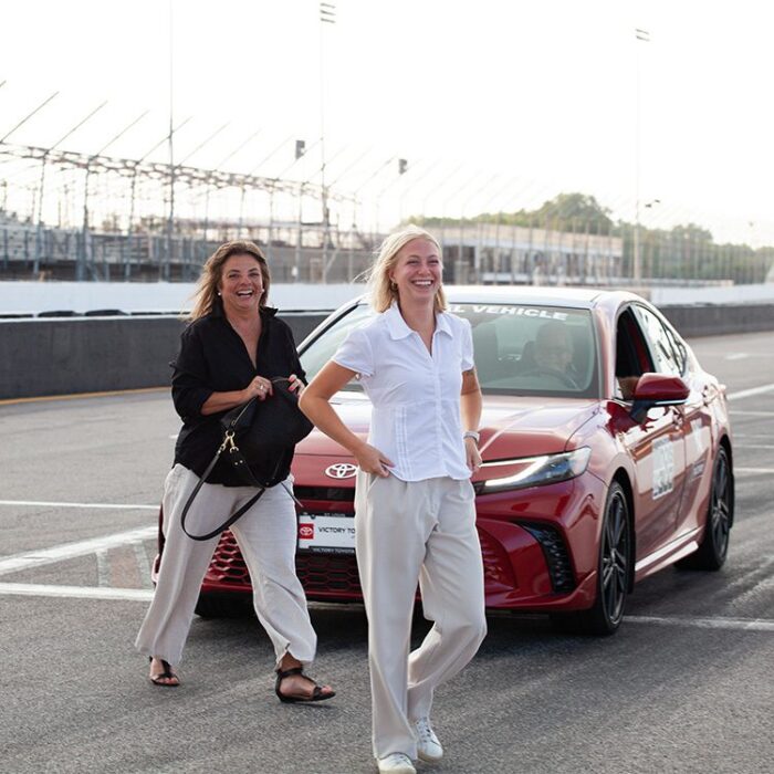 Two Cork Tree Creative team members smiling in front of race car at race track