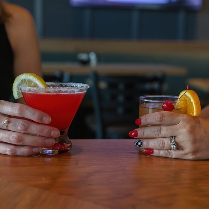 Closeup of two hands holding cocktails at bar of Park North Golf Club